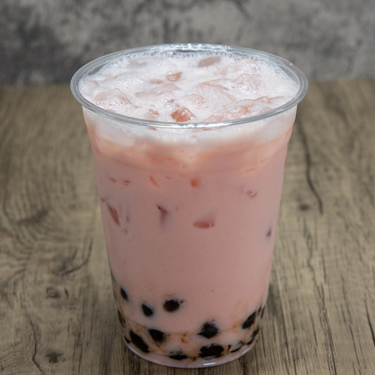 Pink bubble tea with black tapioca pearls in a clear plastic cup on a wooden surface.